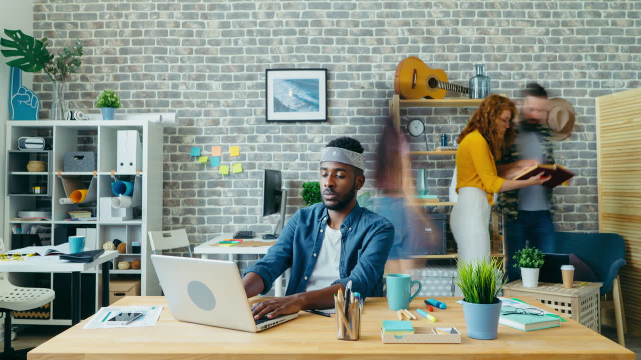 Busy Office Scene with Man Working on Laptop