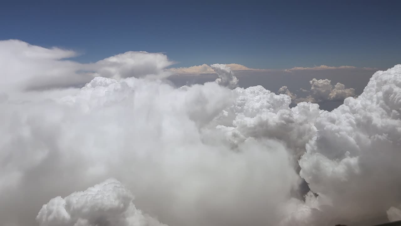 An immersive pilot’s view from inside a jet airplane cockpit while flying through stormy skies full of threatening cumulonimbus storm clouds under a blue sky. Ultra-realistic aerial shot.