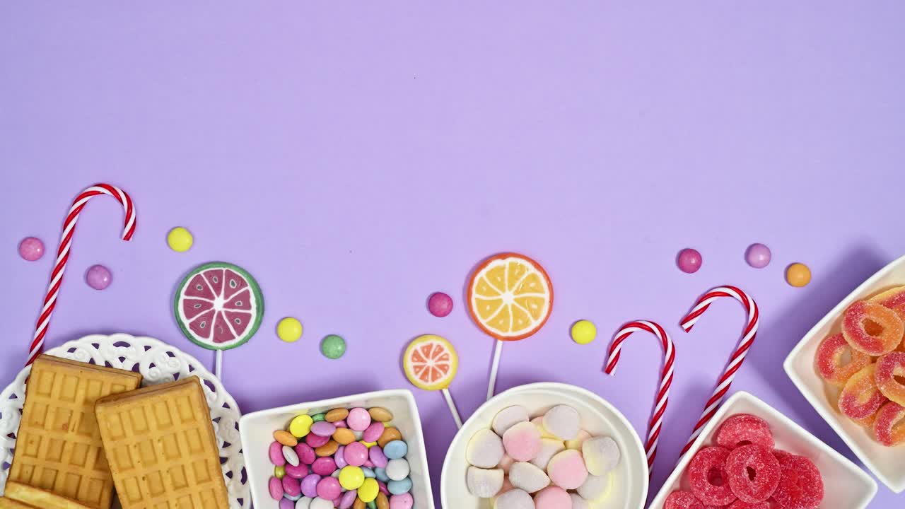 dulces de goma dulces de chocolate y piruletas se mueven en la parte inferior del fondo púrpura pastel. detención de movimiento plana