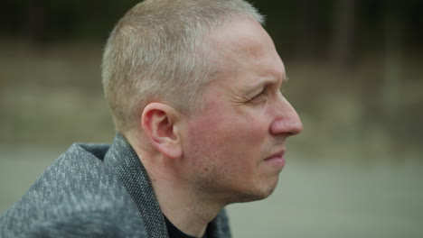 a close-up view of a man's face, displaying a contemplative expression, he is wearing a grey blazer, with a blur background