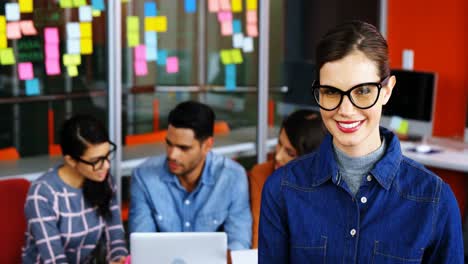 Smiling-female-executive-using-digital-tablet-while-colleagues-discussing-over-laptop