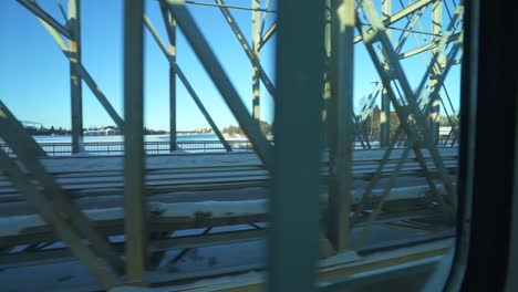 vista a través de una ventana de tren viajando sobre un puente cubierto de nieve, con un paisaje de invierno sereno a su alrededor