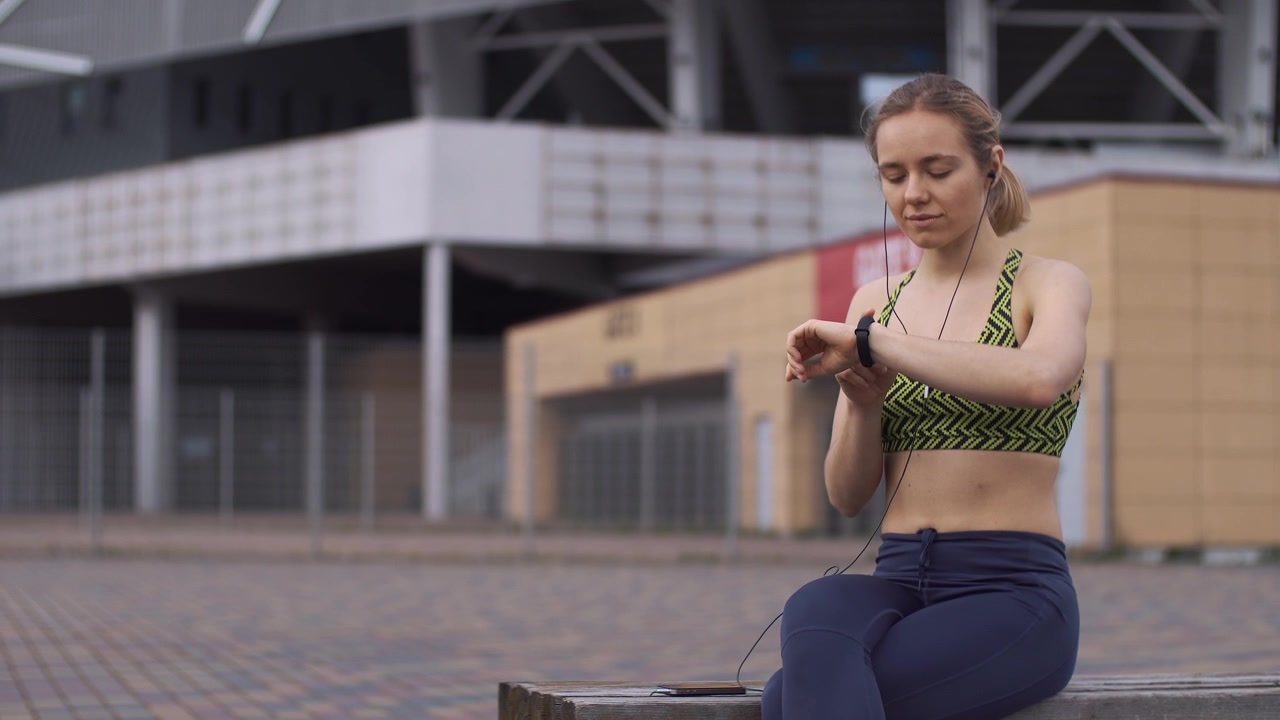 Young Woman Checking Smartwatch and Listening to Music Outdoors