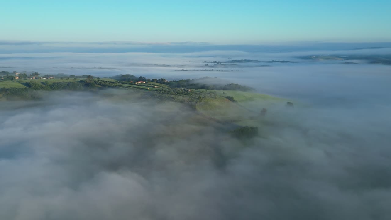 imágenes aéreas que capturan la cima de una colina por encima de la niebla al amanecer, con villas toscanas y un olivar bañado en una cálida luz dorada, ofreciendo una vista serena y pintoresca.