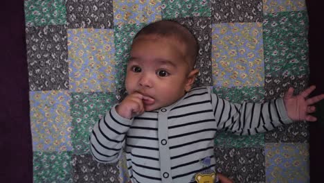 Overhead-View-Of-Adorable-4-Month-Old-Indian-Baby-Boy-Laying-On-Mat-On-The-Floor-Sucking-His-Right-Fingers