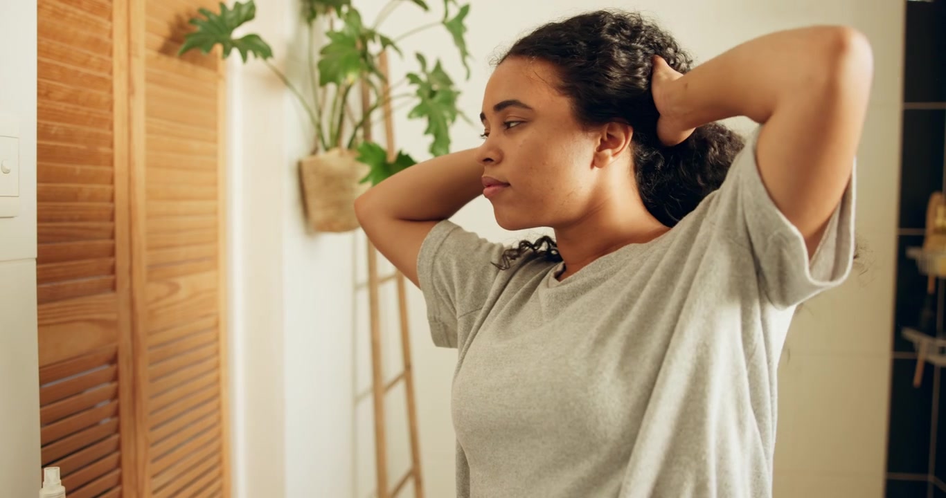 Young Woman Styling Her Curly Hair in Front of a Bathroom Mirror