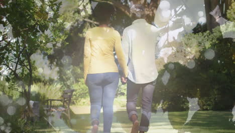 animation of leaves over african american couple walking in garden