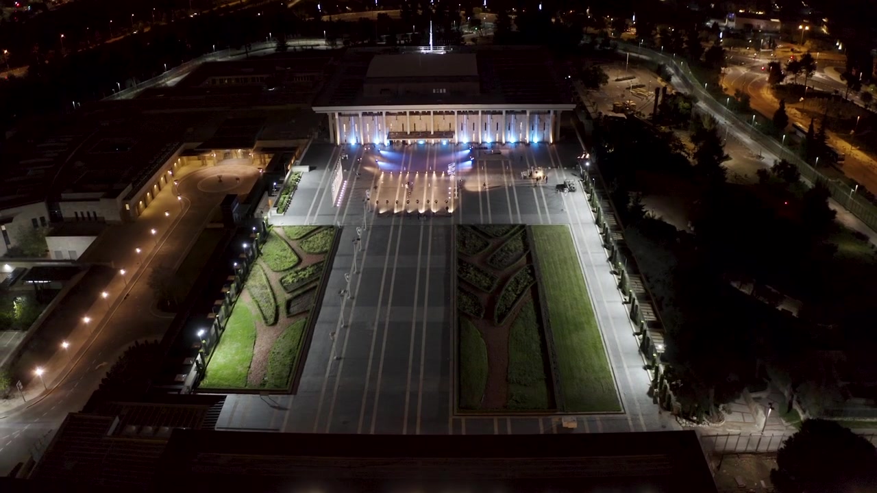 High angle vista of illuminated government complex forecourt and manicured lawns during evening hours in Jerusalem