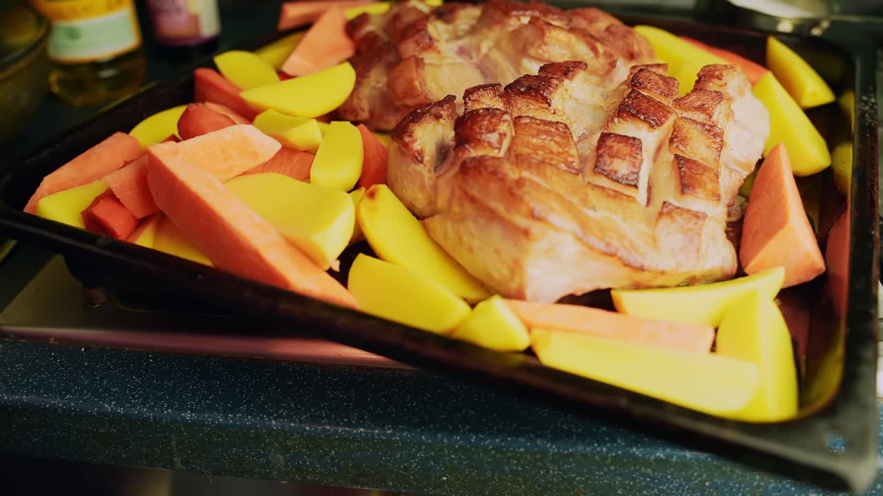 Primo piano di arrosto di lonza di maiale con cotenna croccante in una pirofila, circondato da spicchi di patate e pezzi di patata dolce per un sostanzioso pasto invernale festivo