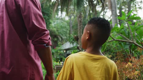 Happy-senior-african-american-man-with-his-grandson-walking-together-in-garden