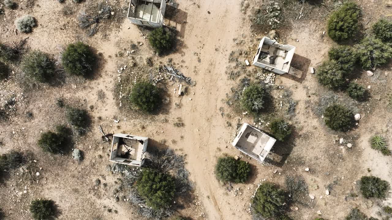 Rovine di edifici abbandonati, strutture in cemento distrutte dalla violenza delle gang dei cartelli nell'alto deserto della California meridionale in una giornata nuvolosa con un'atmosfera apocalittica. Ripresa aerea dall'alto con carrello a 60fps.