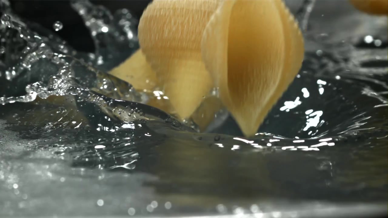 Rohe Conchiglie-Nudeln fallen in Zeitlupe in spritzendes Wasser