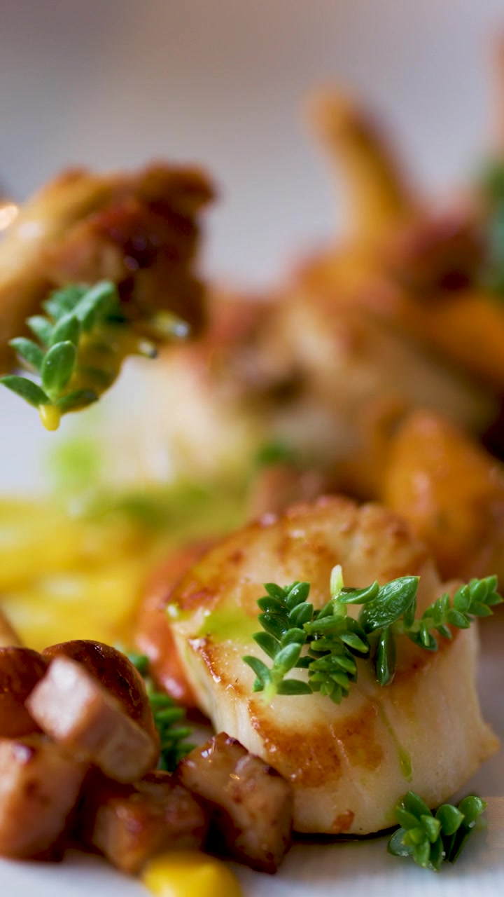 Un primo piano di capesante gourmet guarnite con alghe e verdure, mentre una forchetta solleva un boccone. L'illuminazione naturale e brillante e la profondità di campo ridotta esaltano l'impiattamento elegante