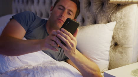 man in bed putting in wireless earphones connected to mobile phone before going to sleep