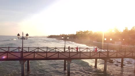 Puesta-De-Sol-Desde-Drone-Hermosa-Vista-Del-Muelle-Y-Parejas-Caminando-Sobre-él