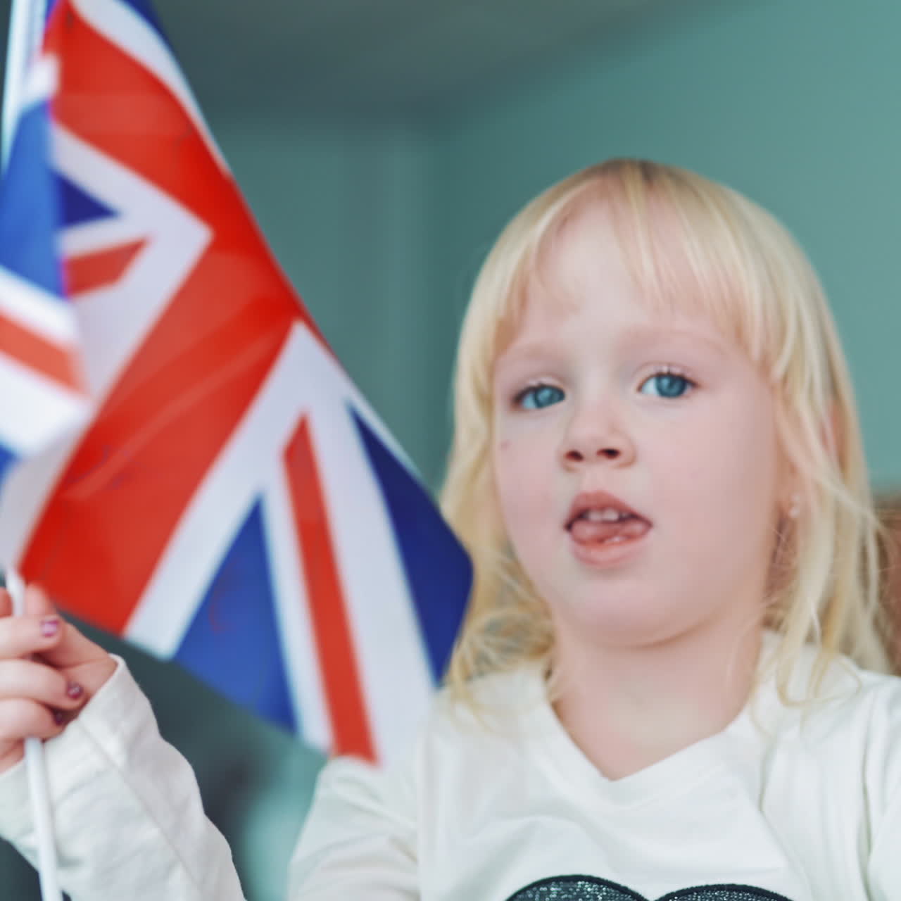 Cute little girl playing with British flag. English flag with three red crosses on blue and white background. Flag of Great Britain in child's hands indoors.