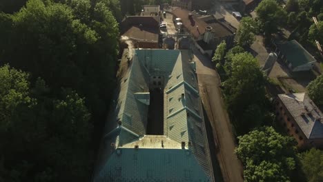 A-historic,-vintage-brewery-with-smoking-chimneys,-surrounded-by-green-trees-during-summer-in-Poland's-Silesia-region