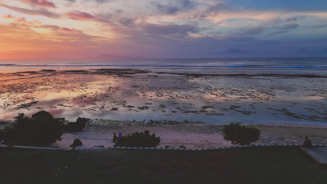 clip de avión no tripulado que desciende de una hermosa puesta de sol multicolor que se refleja en el mar tranquilo y el arrecife de coral, en el parque nacional de alas purwo, java, indonesia