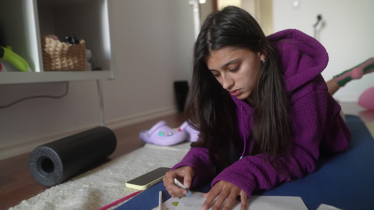 Mujer joven tumbada en el suelo estudiando y escribiendo en casa