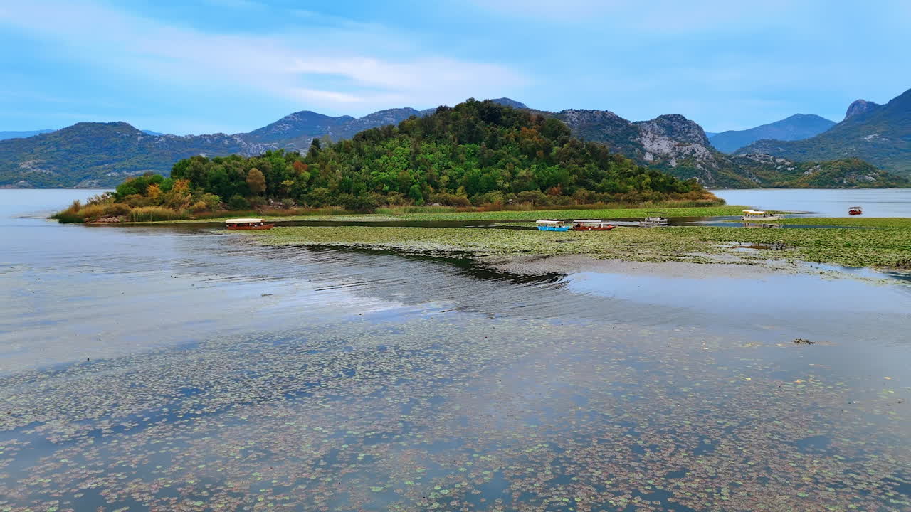 Water lilies cover the vast waterscape of the lake in the mountains. Approaching the boats on the water near the rocky island covered with greenery