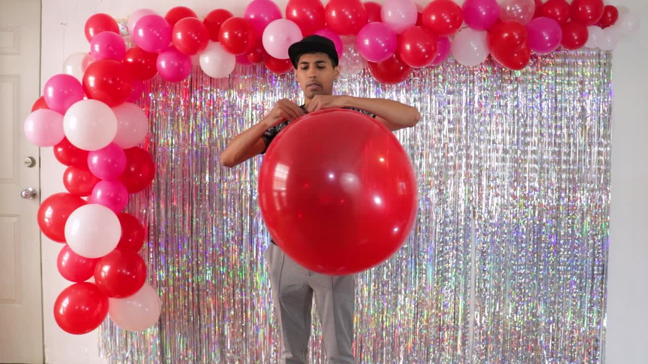 hombre latino atando un gran globo rojo en una habitación decorada para el día de san valentín