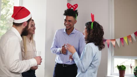 grupo multiétnico de trabajadores de oficina felices sosteniendo copas con vino espumoso y hablando durante la fiesta de navidad en la oficina