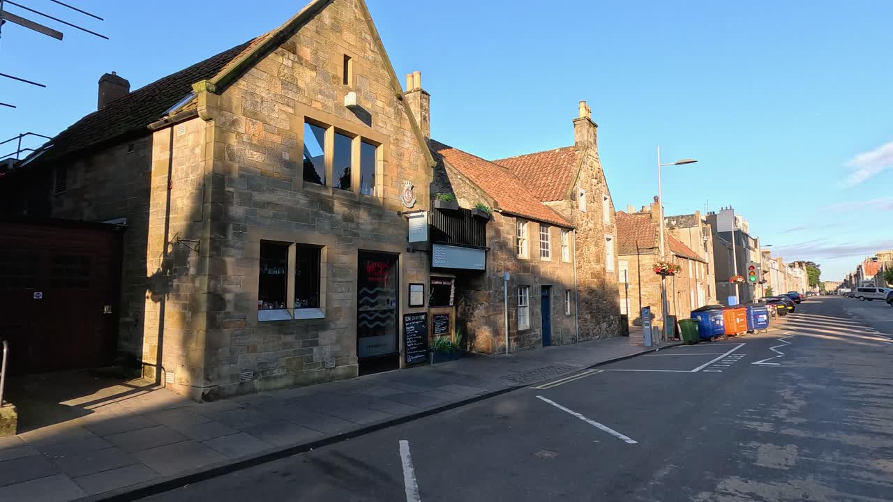 Camera moves along quiet old town street, passing gothic church and sunlit traditional buildings
