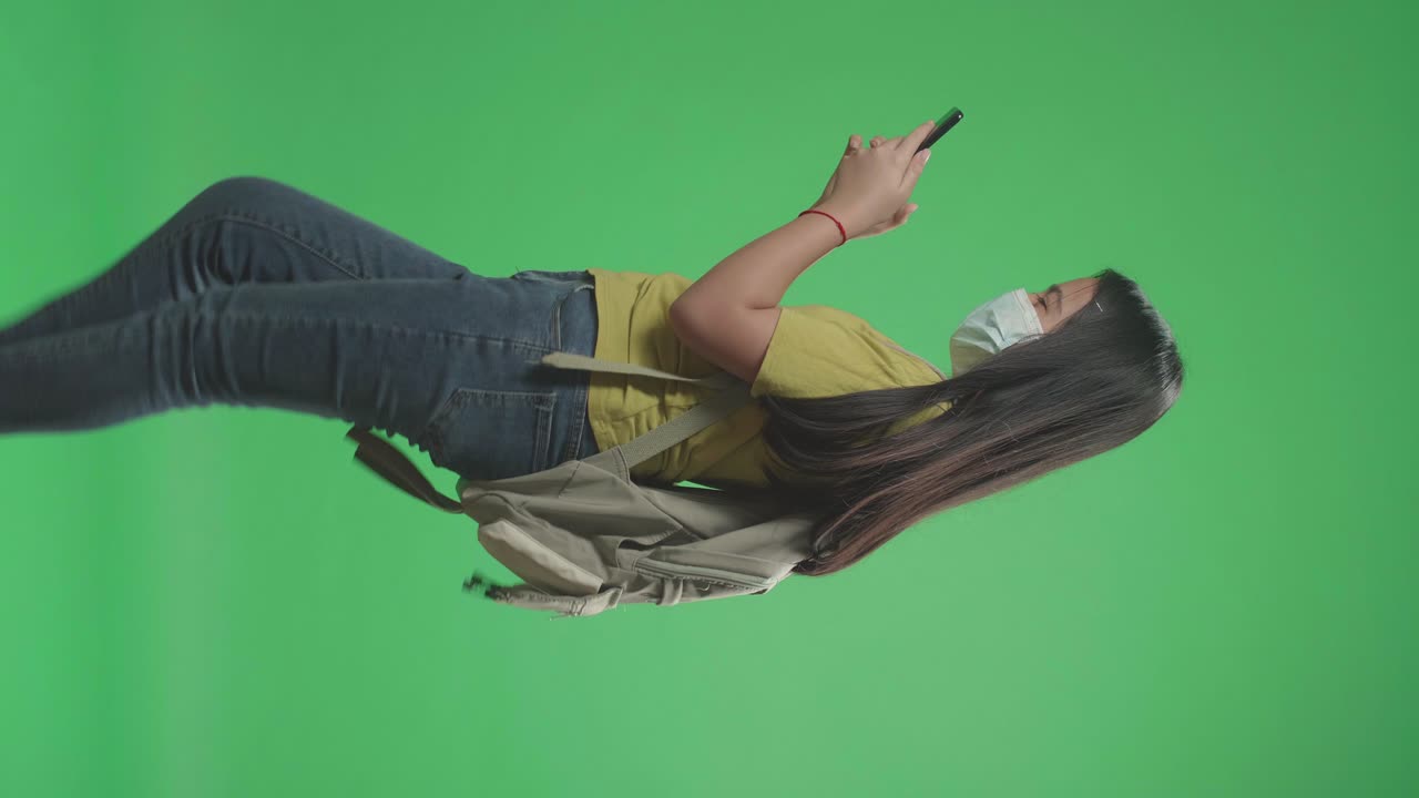 Side View Of Asian Girl Student Wearing A Mask And Use Mobile Phone While Walking To School On Green Screen Chroma Key