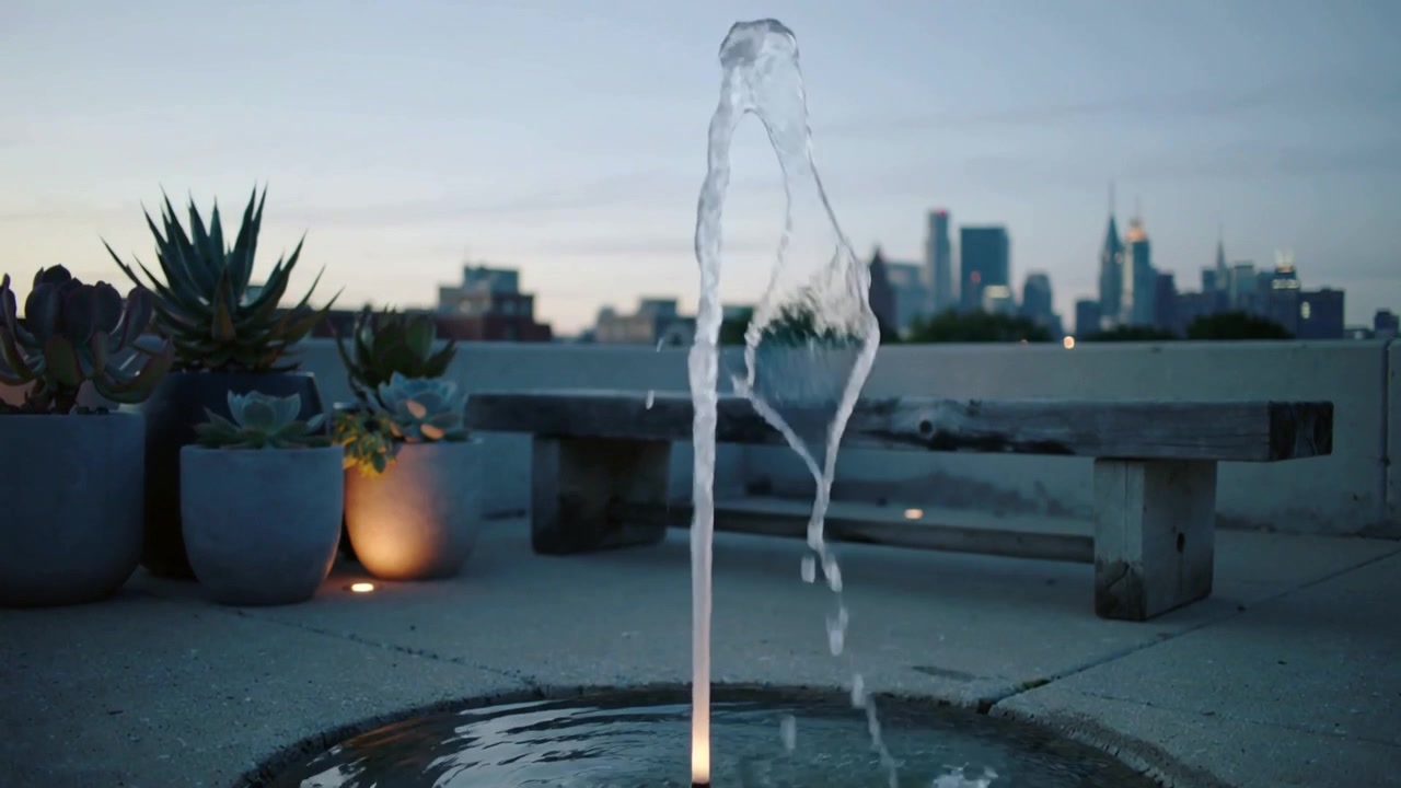 Bomba activándose, chorro de fuente elevándose y cambiando de forma en una terraza en la azotea con estanque y suculentas.