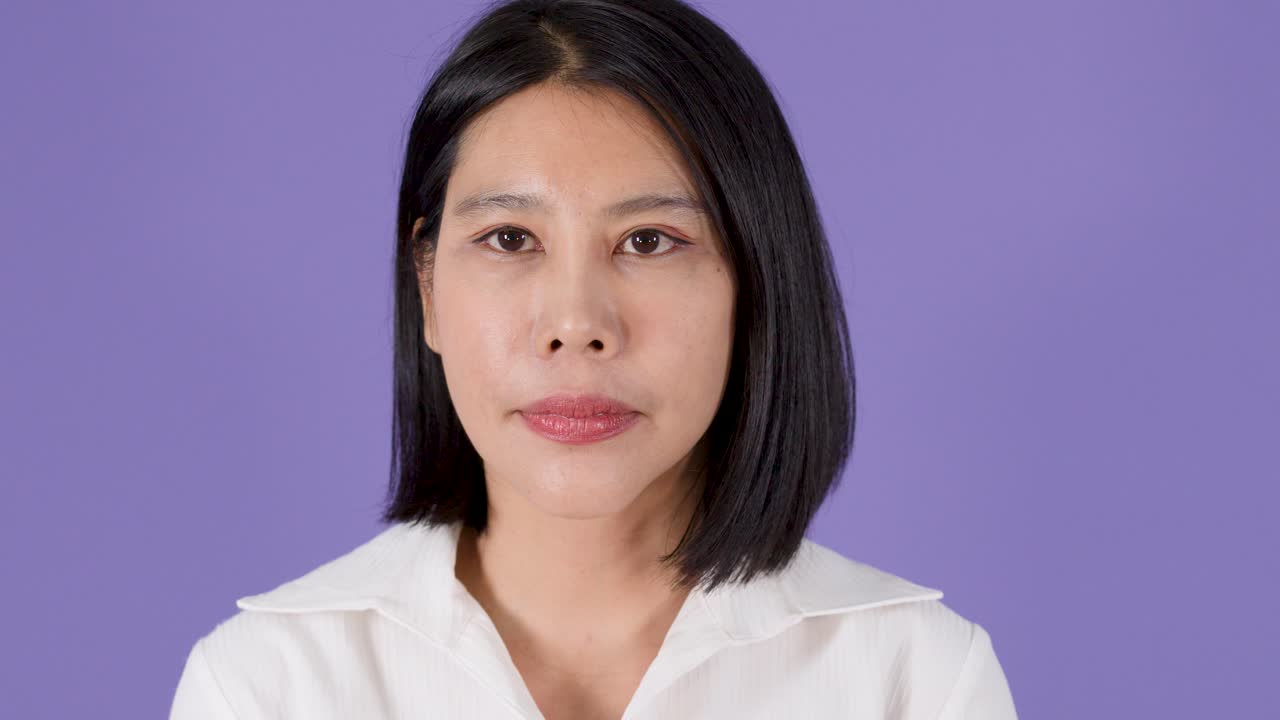 Bidikan medium seorang wanita Asia sedang berpikir dan melihat ke atas dengan latar belakang ungu