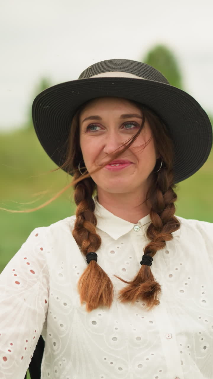 드레스와 검은 모자를 입은 여자가 녹색 에 앉아 따뜻하게 미소 짓고 있습니다. 야외 설정은 그녀의 즐거운 표정을 강조합니다.