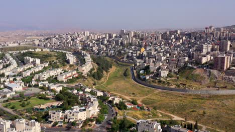 aerial view of a city divided by a security barrier, likely in the middle east