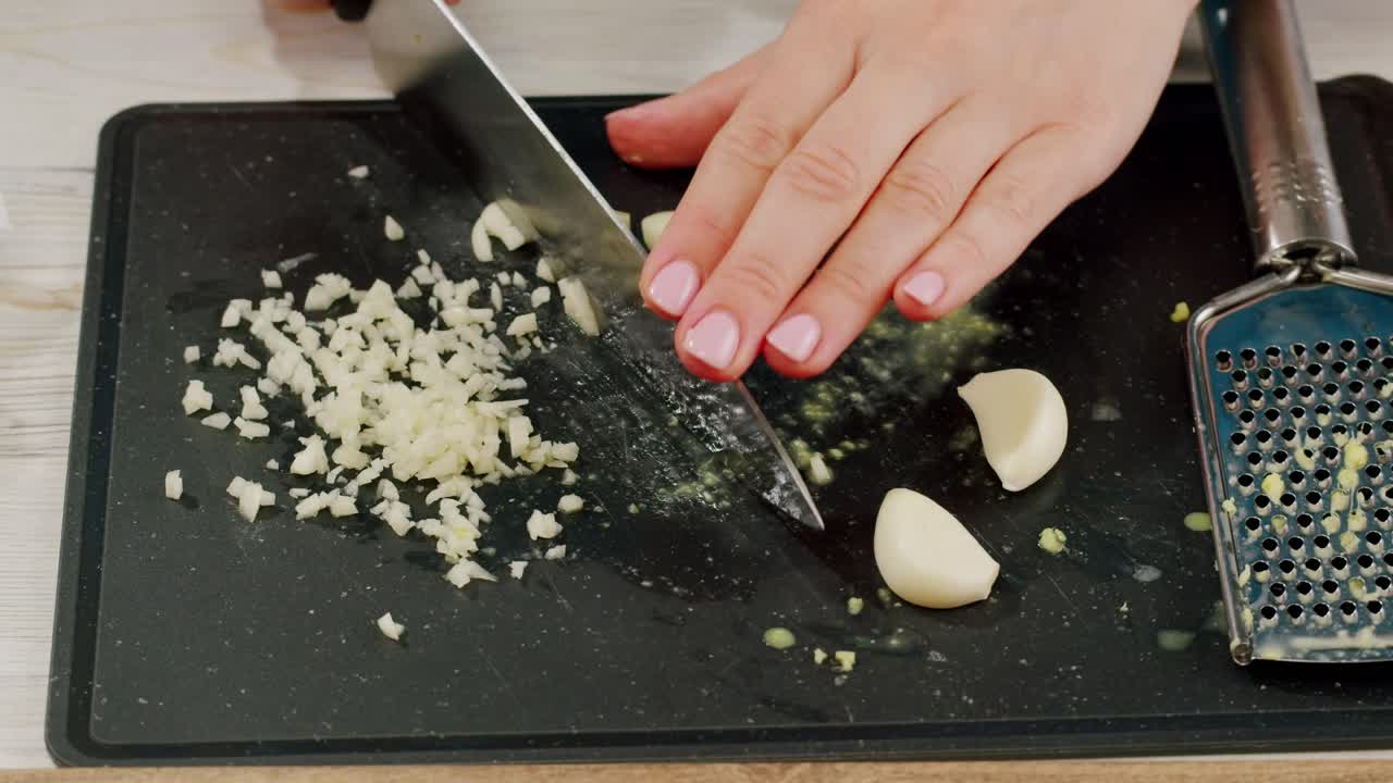 Woman chopping garlic on wooden cutting board at domestic kitchen. High quality 4k footage