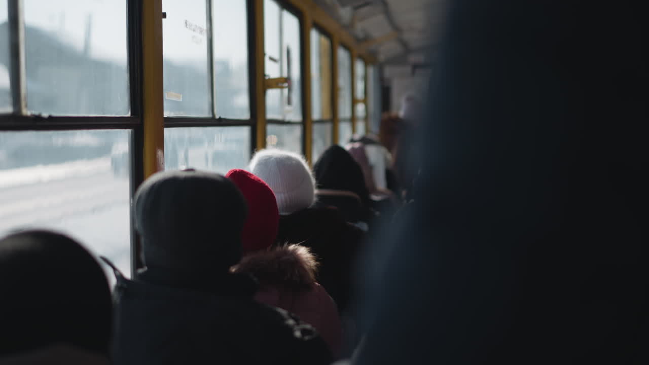 Inside moving bus packed with winter passengers, rows of hats and fur hoods fill frame while sunlight washes fogged windows, subtle motion chatter suggest daily commute through cold city streets