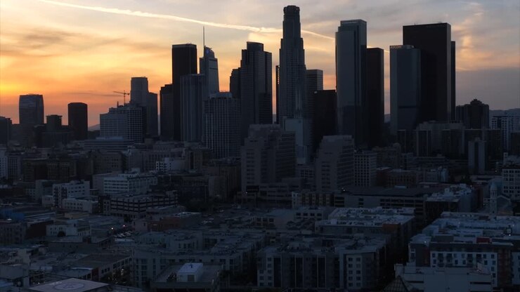 Downtown Los Angeles bei Sonnenuntergang, Luftaufnahme von Wolkenkratzern, Turmsilhouetten und orangefarbenem Himmel im Hintergrund, Pedestal-Drohnenaufnahme