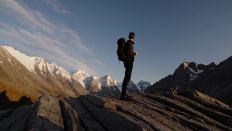 hiker with backpack stands on rocky peak overlooking vast snowy mountains