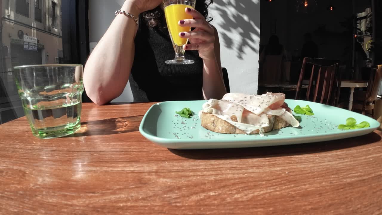 Donna che beve succo d'arancia e mangia toast con prosciutto al bar