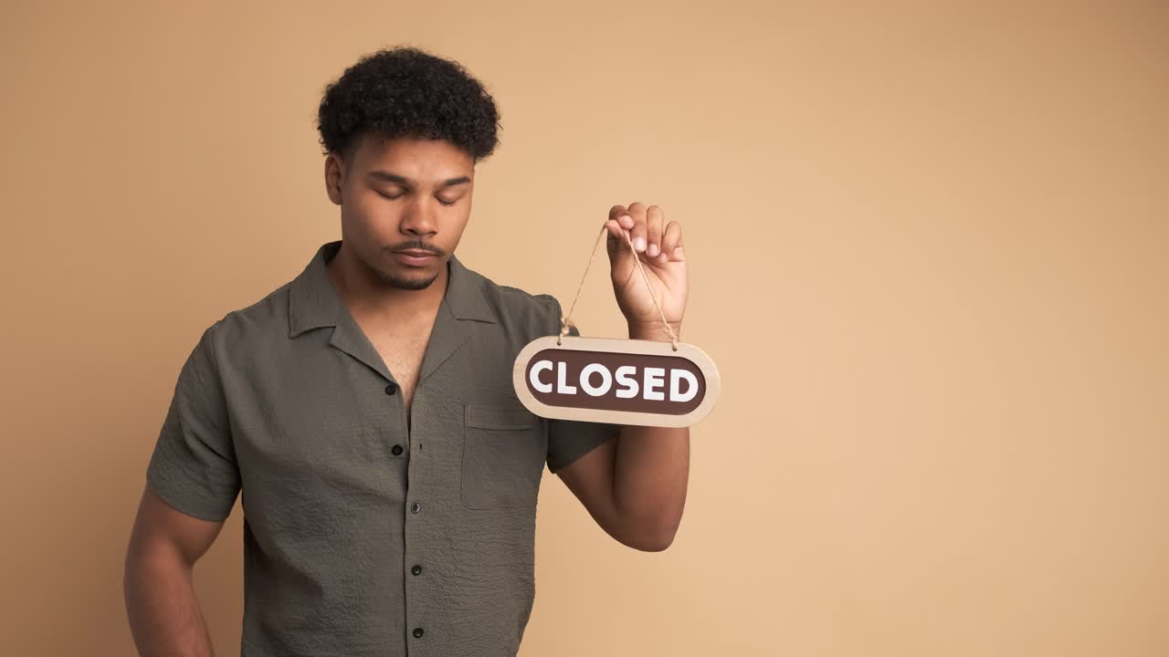 Upset young man with closed sign in beige studio