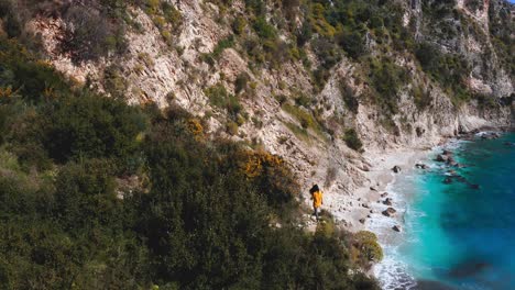 Fearless-woman-walking-along-edge-of-a-cliff-above-blue-turquoise-water-beach