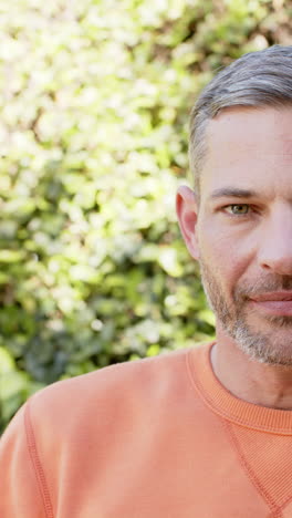 vertical video of half face of happy caucasian man standing and smiling in sunny garden