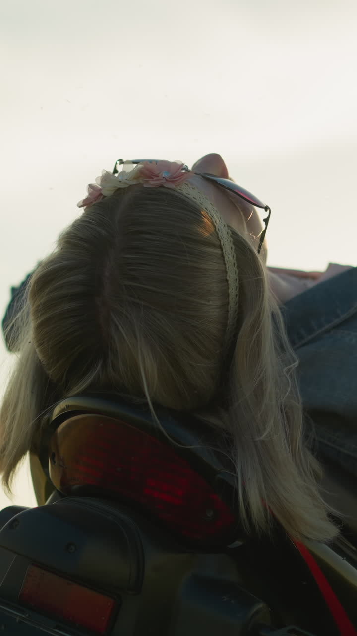 una mujer con gafas de sol descansa en el asiento de una bicicleta con la cara hacia el cielo, tocando brevemente su cabello y luego bajando la mano