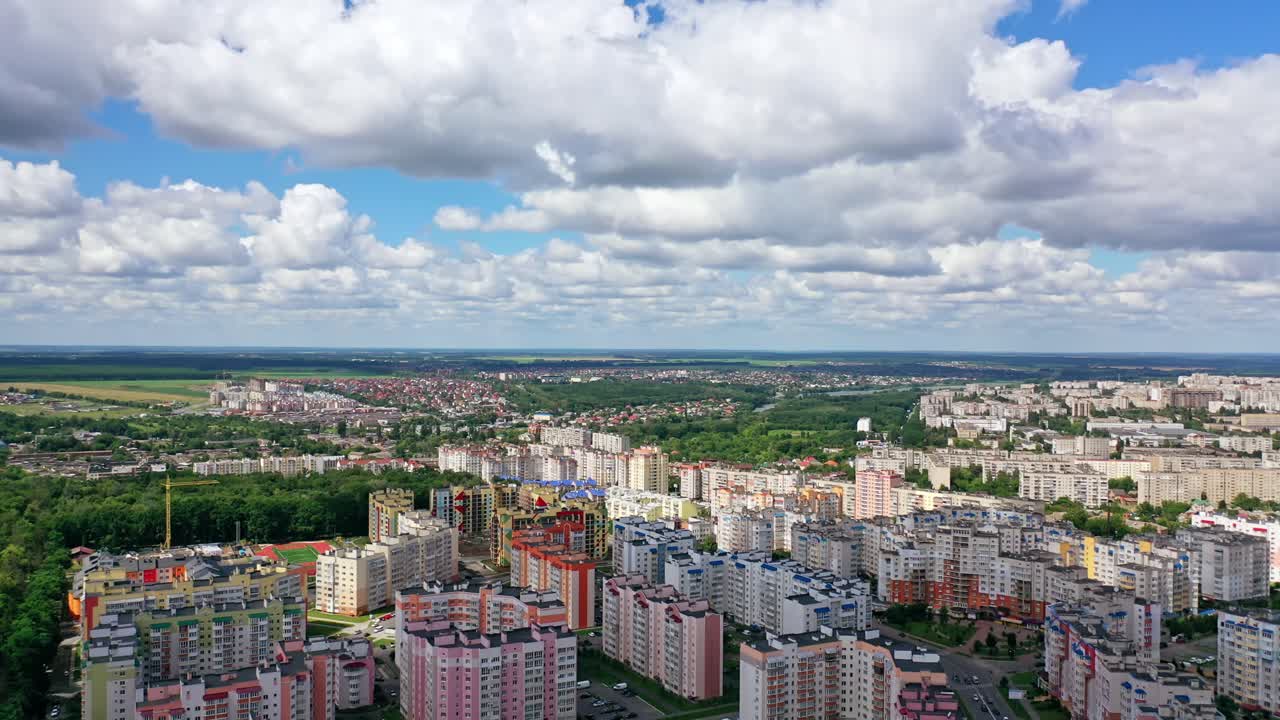 Urban background under beautiful sky. Modern city with high-rise buildings on green fields background. Aerial view. Camera rising up.