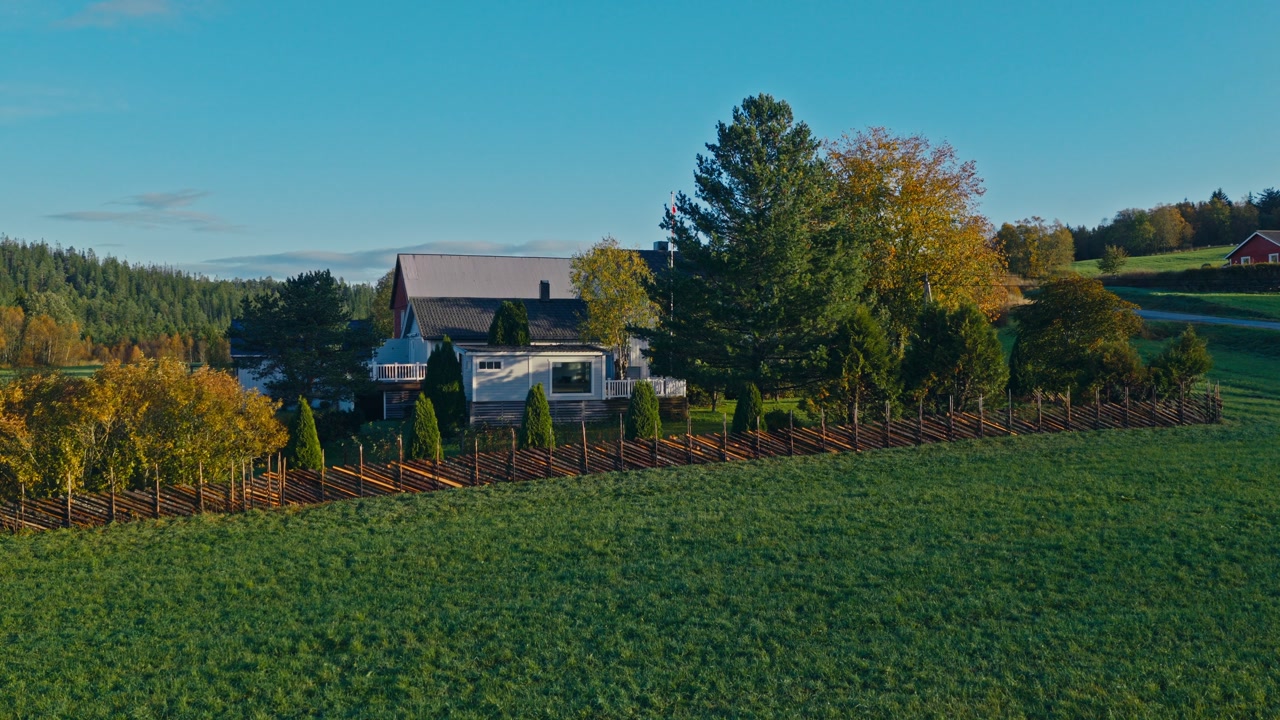A Charming Farmhouse Sits Nestled in the Greenery, Surrounded by a Wooden Fence and Vibrant Autumn Trees - Drone Flying Forward