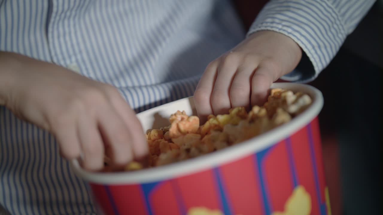 la mano del niño tomando palomitas de maíz de la caja de papel en el cine. los niños toman palomitas de maíz caramelo