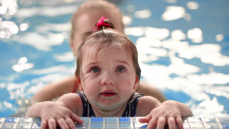 little baby girl while swimming in the pool looking at the camera standing on the side in the water and smiling