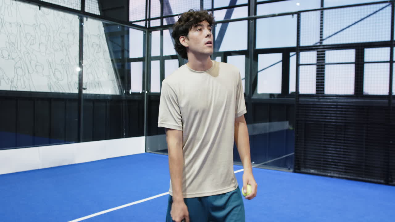 Man practicing padel tennis swing on indoor court, focusing on technique, copy space
