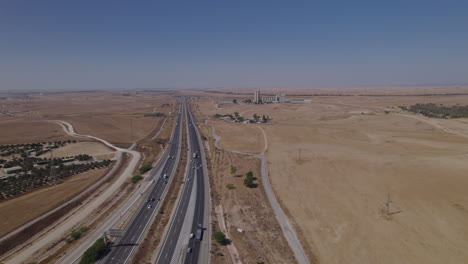 Toma-Aérea-Cerca-De-Una-Carretera-En-Una-Zona-Seca-Y-Desértica,-Una-Zona-No-Urbana,-Los-Suburbios-De-La-Ciudad,-Algunos-Edificios-De-Los-Terratenientes-Y-Una-Antigua-Fábrica-En-La-Distancia