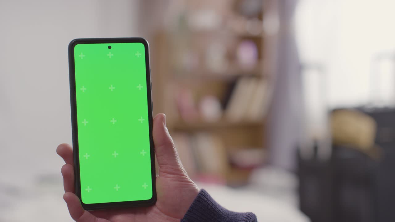 초록색 화면 휴대폰을 들고 있는 집에 있는 사람. 배경 1에 여름 휴가를 위해 짐을  ⁇ 고 있다.