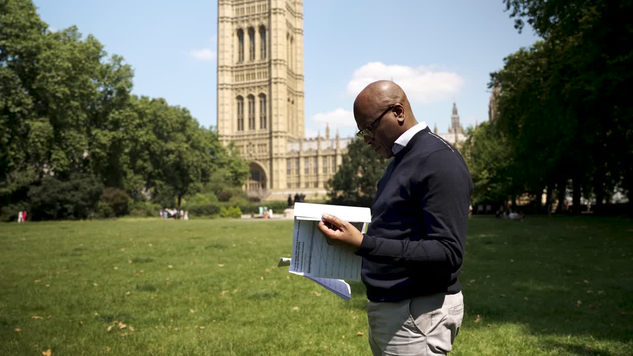 Bald professional reading papers in Victoria Gardens, with Westminster as a backdrop