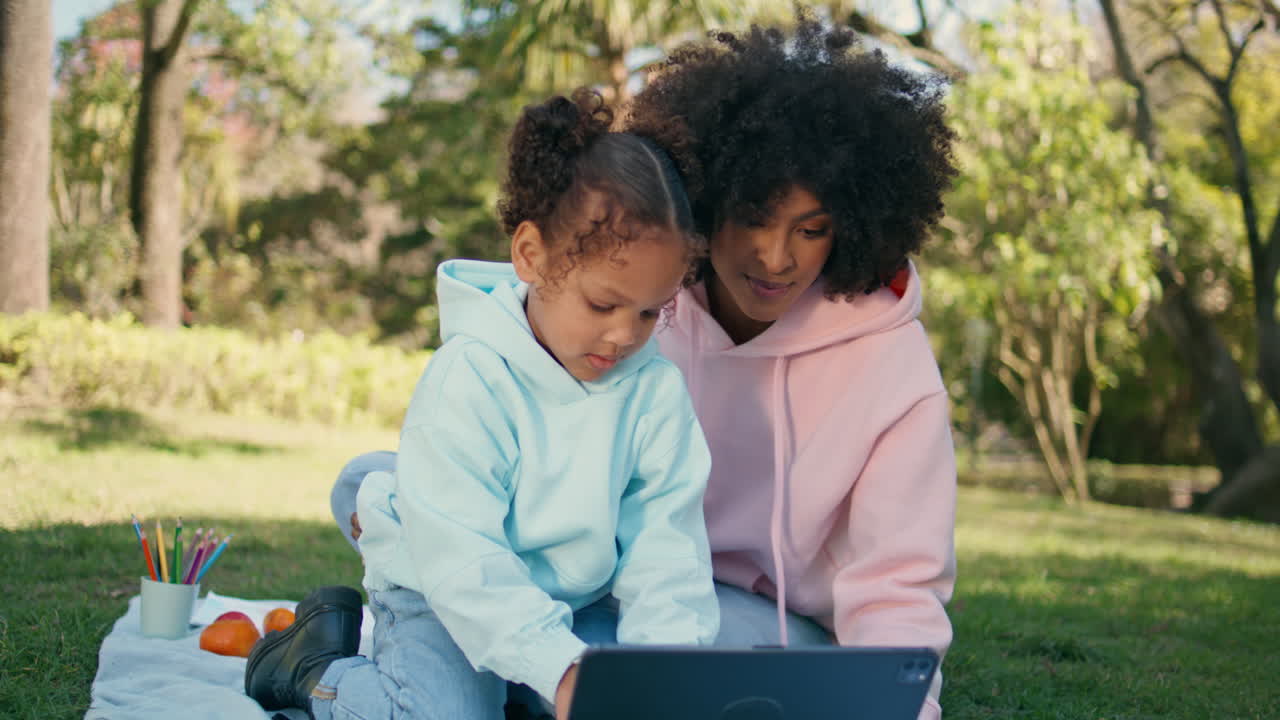 Curly child playing tablet sitting picnic with mother close up. Family weekend
